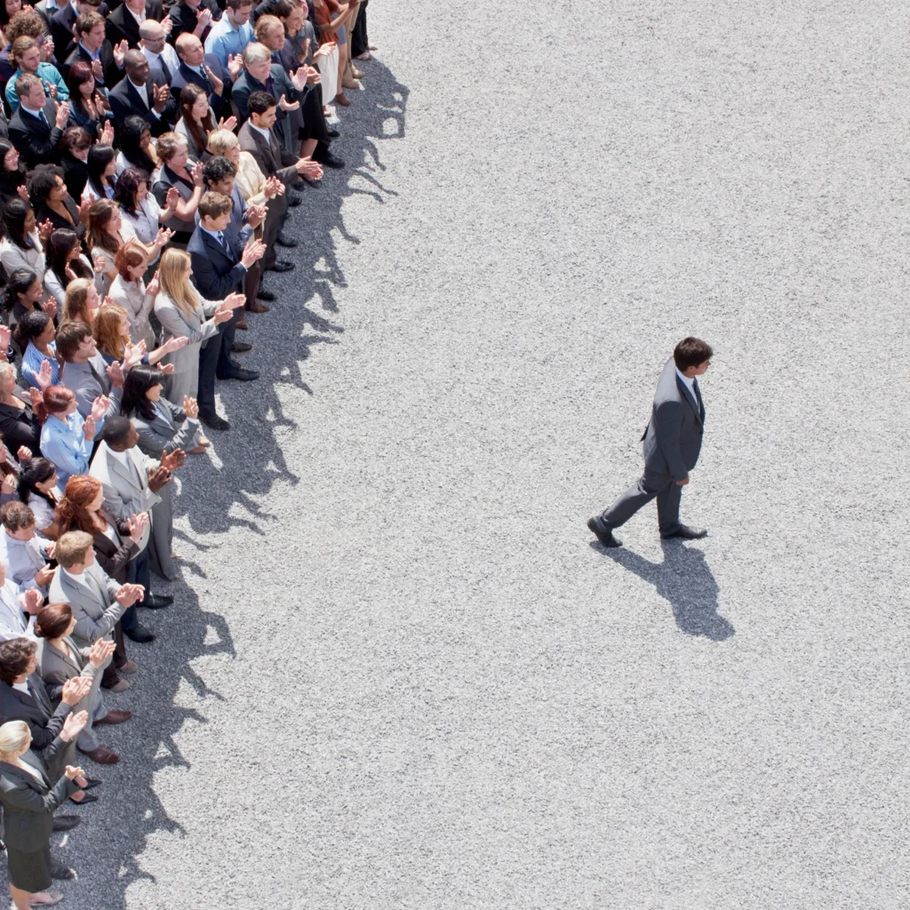 Businessman walking alone while crowd applauds