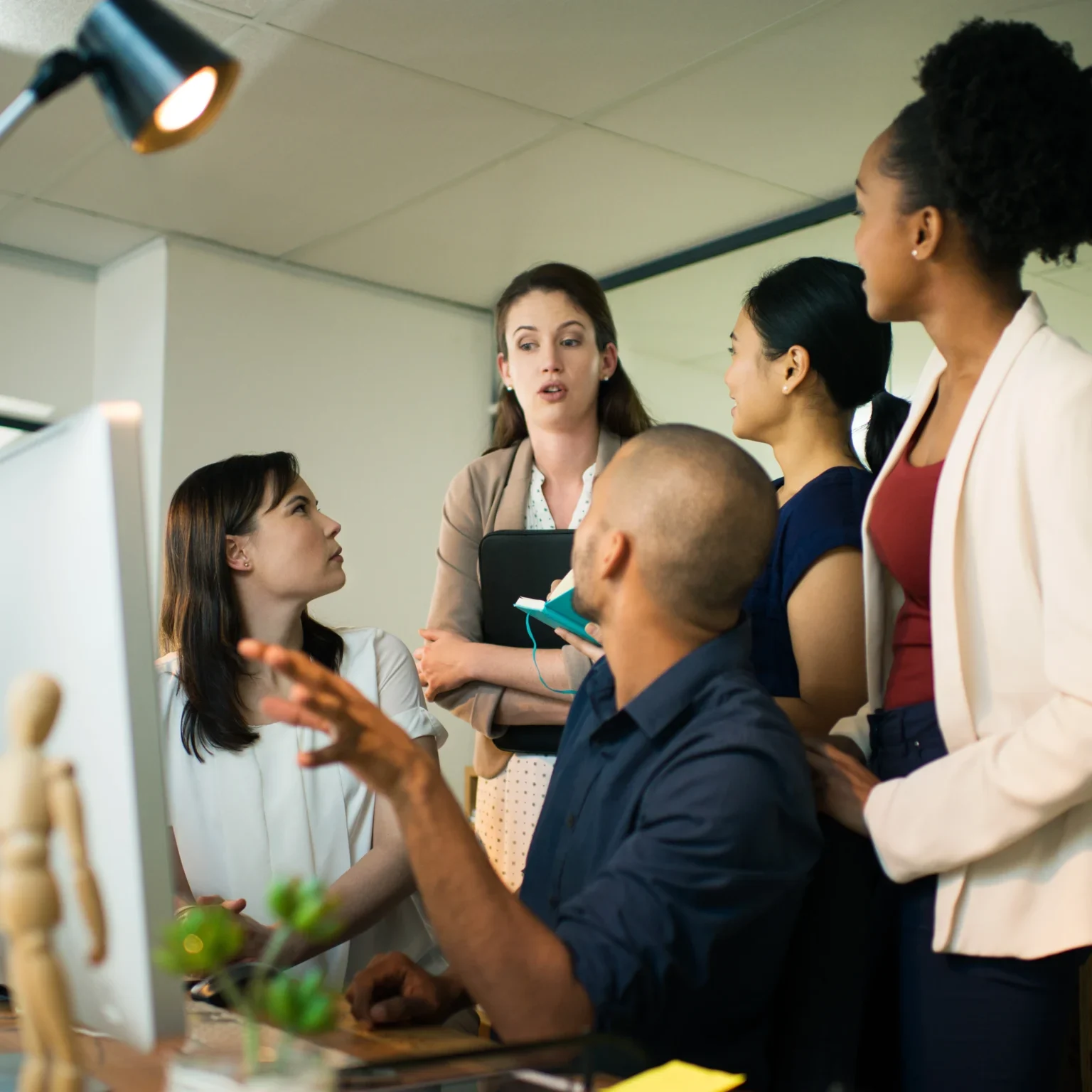 A team of colleagues gathered around a computer monitor, actively discussing a project in an office.